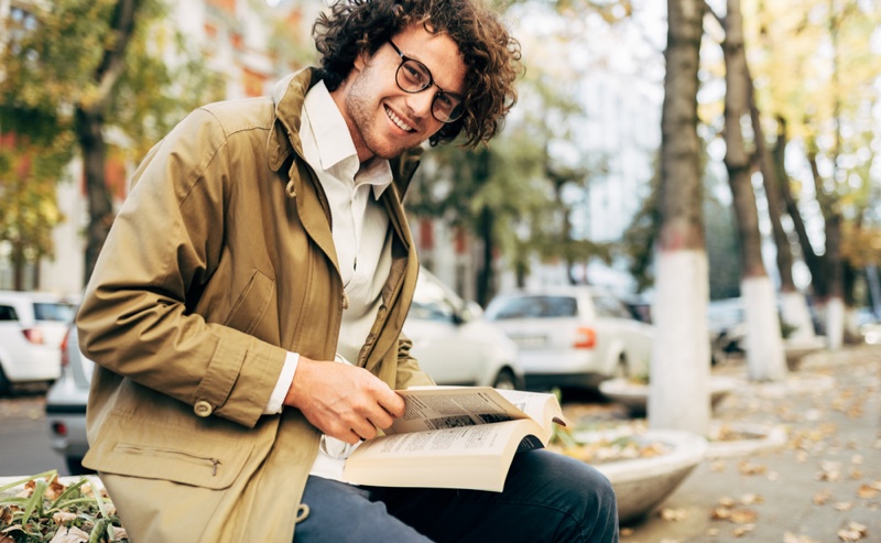Smiling Male Model Reading Book Glasses Jacket Outdoors
