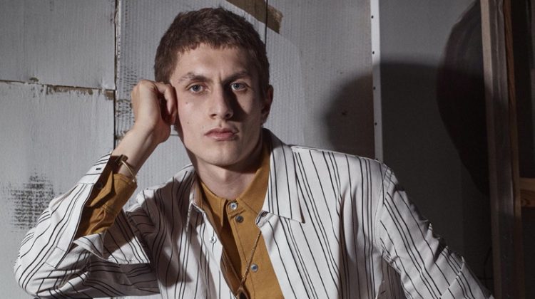 Henry Kitcher fronts Zara's fall-winter 2020 men's campaign. Sitting for a portrait, the top model wears a mixed stripe shirt over a button-down with trousers. A brown leather belt and loafers bring his look together.