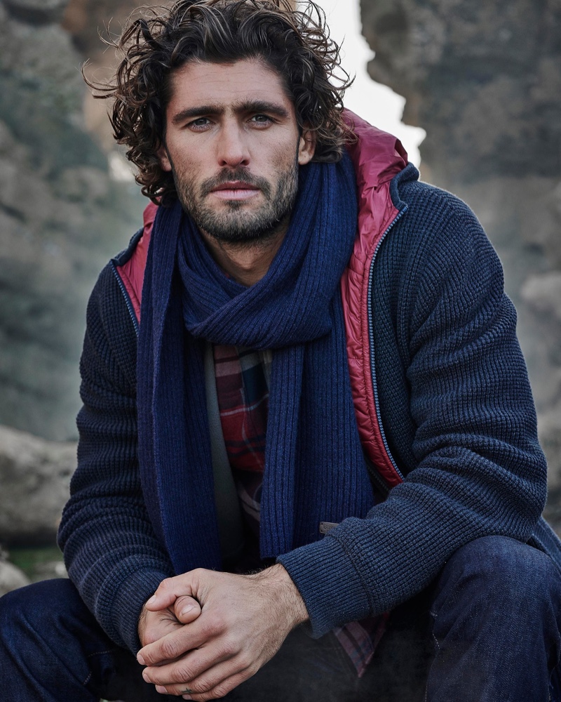 Layering in navy tones, Alex Libby wears a hooded knit jacket, scarf, and flannel shirt from Barbour.