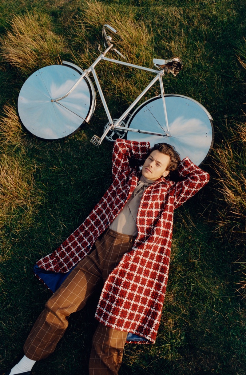 Laying in the grass, Harry Styles wears a Gucci overcoat with a shirt and pants for Vogue.