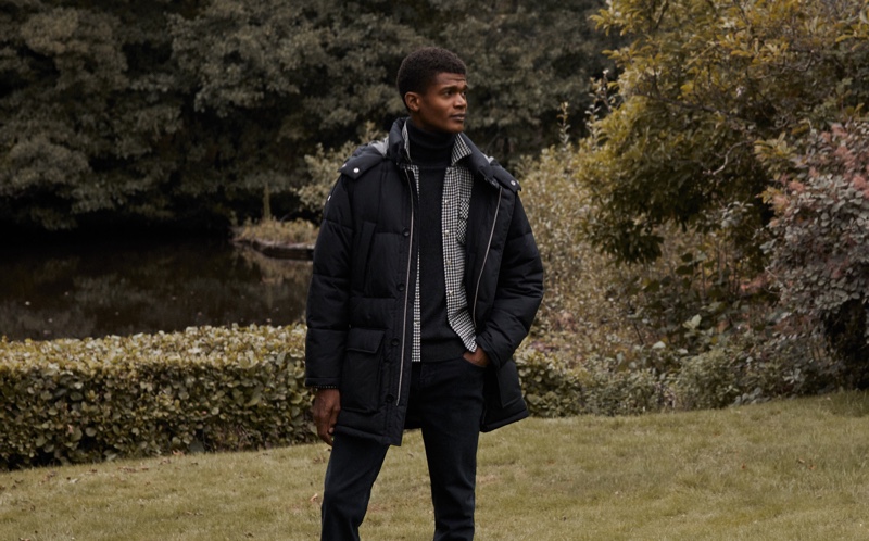 O'Shea Robertson wears a down coat with a shirt, sweater, and jeans from Reiss for the brand's fall-winter 2020 campaign.