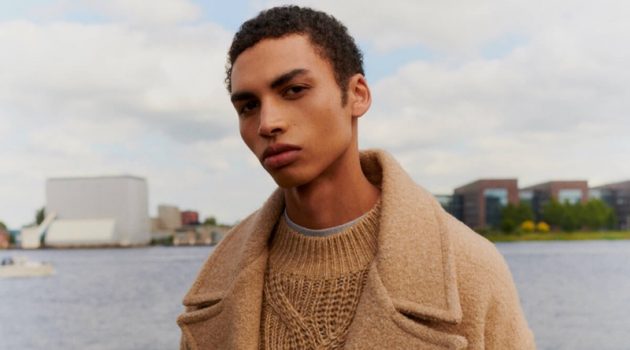 Sol Goss dons a chic winter coat with a cable-knit sweater from Scotch & Soda.