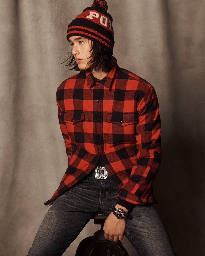 Peter Meyer dons a red and black buffalo check shirt with a knit pom beanie and distressed jeans from POLO Ralph Lauren's holiday 2020 collection.