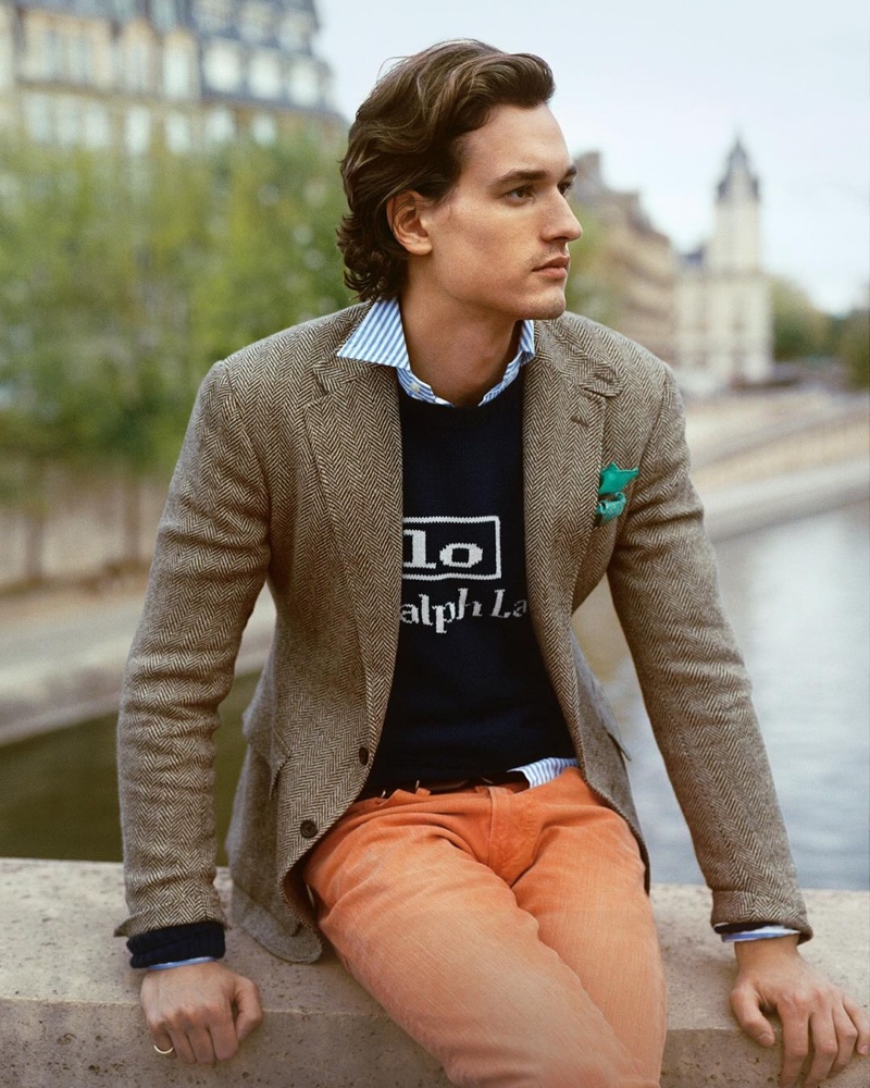 A regular face of POLO Ralph Lauren, Jegor Venned wears orange jeans with a logo knit sweater, tweed blazer, and striped oxford shirt.