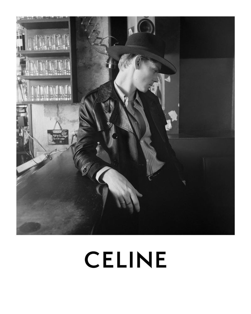 A chic vision, Thomas Brodie-Sangster sports a classic fedora and leather trench coat for Celine's spring-summer 2021 campaign.