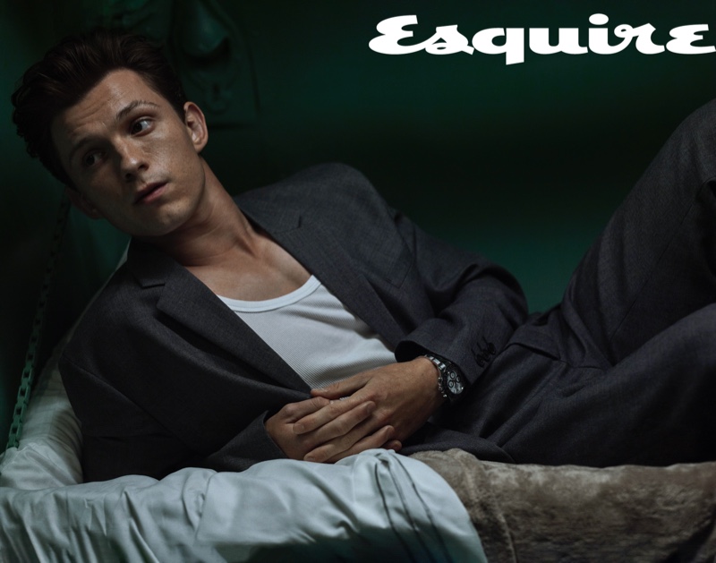 Lounging, Tom Holland dons a Prada suit, Hanes tank, and Rolex watch for Esquire.