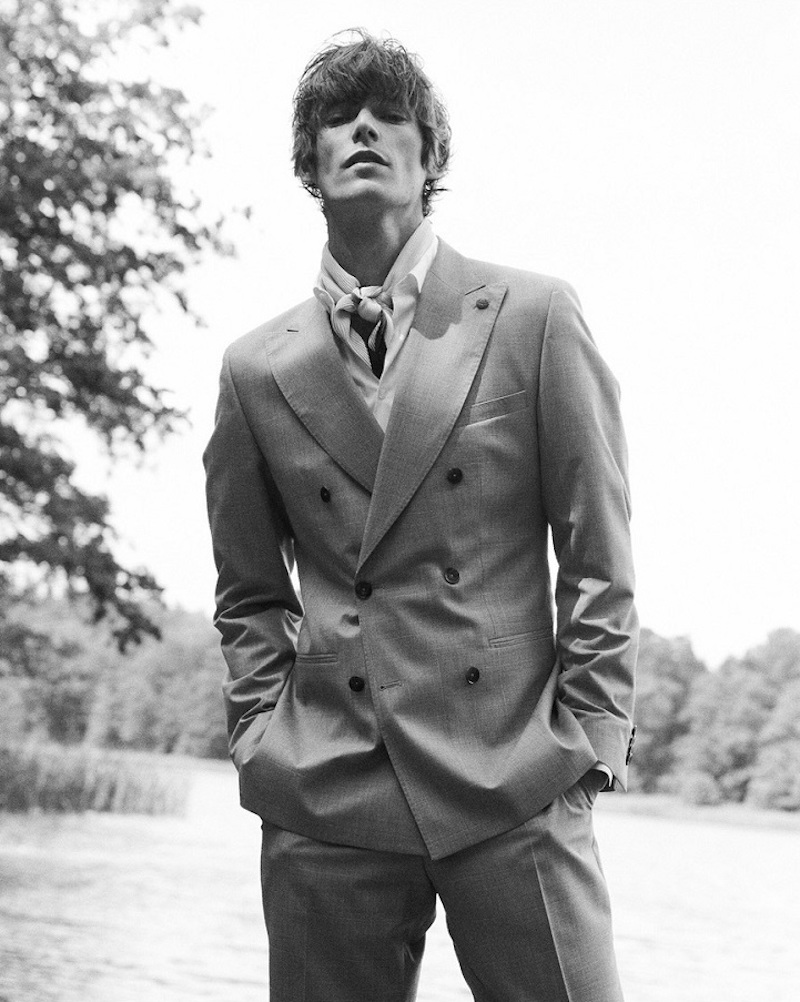 Appearing in a black and white photo, Conrad Leadley models a sharply tailored double-breasted suit by Club of Gents.