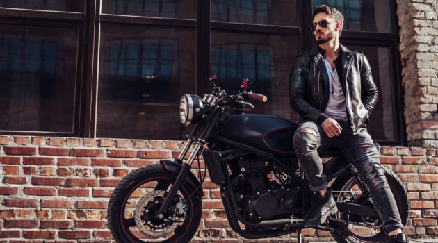 Top Tips to Buy Your First Leather Jacket Online Man in Leather Jacket Posing Against Motorcycle