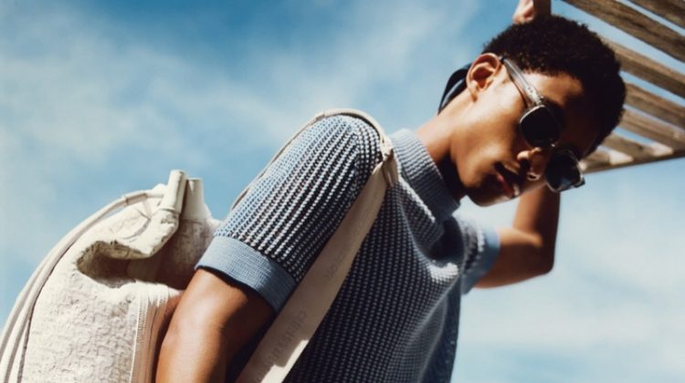 Jecardi Sykes sports a short-sleeve knit, swimwear, and sunglasses from Dior Men's 2021 beachwear collection.