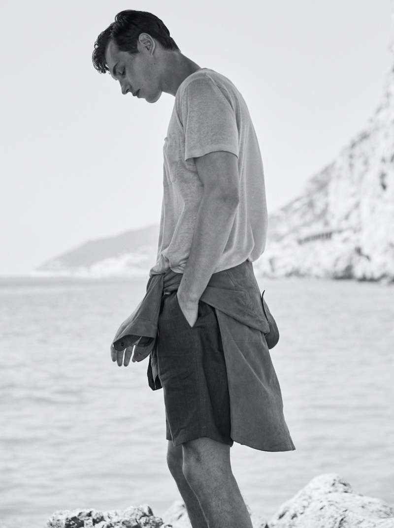 Appearing in a black and white image, Kit Butler dons a suede overshirt, 100% linen t-shirt, and technical cotton poplin Bermuda shorts from Massimo Dutti.