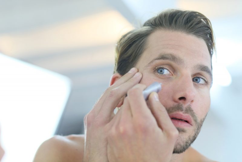 Man in front of mirror using cosmetic cream