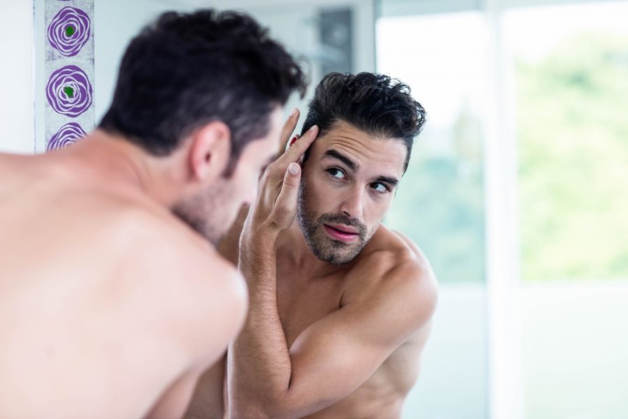 Mens Skincare Handsome man looking at his hair in bathroom