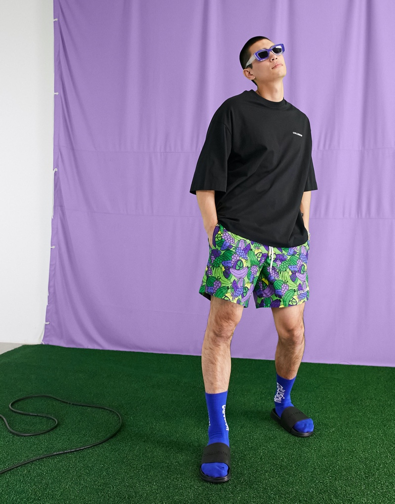 Embracing a sporty look, Del Winder wears ASOS's COLLUSION swim shorts that feature an all-over fruit print.