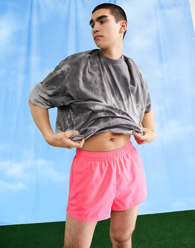 Standing out, model Del Winder sports ASOS's COLLUSION short swim shorts in neon pink.