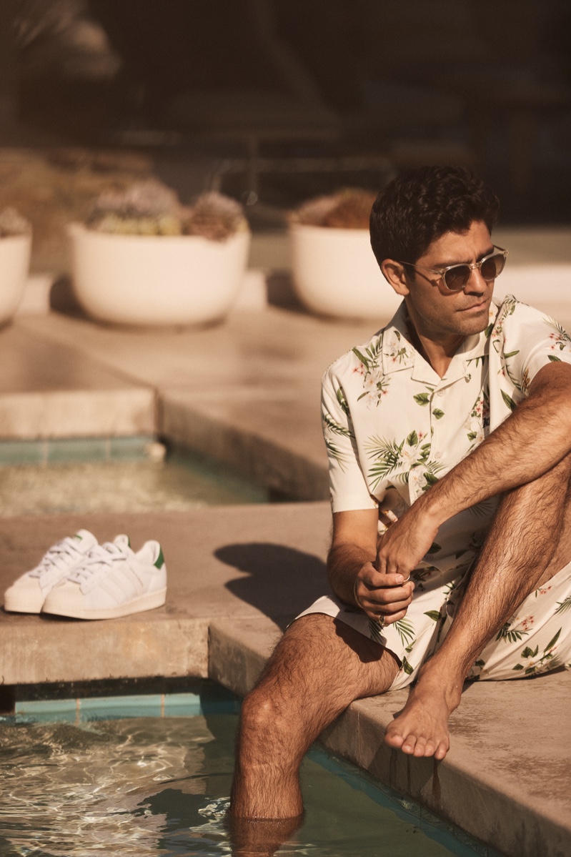 Relaxing poolside, Adrian Grenier wears a matching shirt and shorts with a tropical print for Kith's summer 2021 campaign.