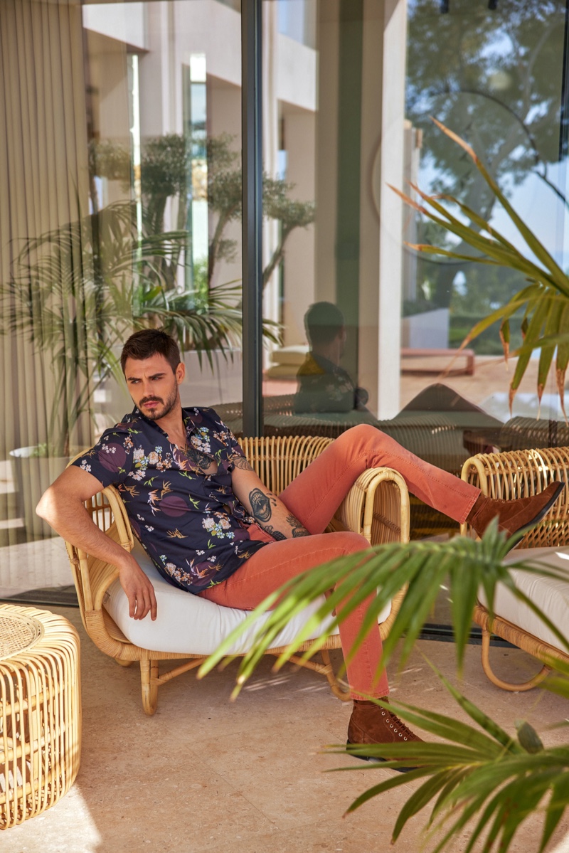 Relaxing, Francesco Monte models a floral print shirt for GUESS' summer 2021 men's campaign.