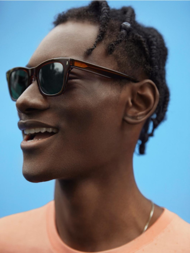 Photographed from the side, Youssouf Bamba takes delight in wearing Warby Parker's Harris sunglasses in Cacao Crystal.