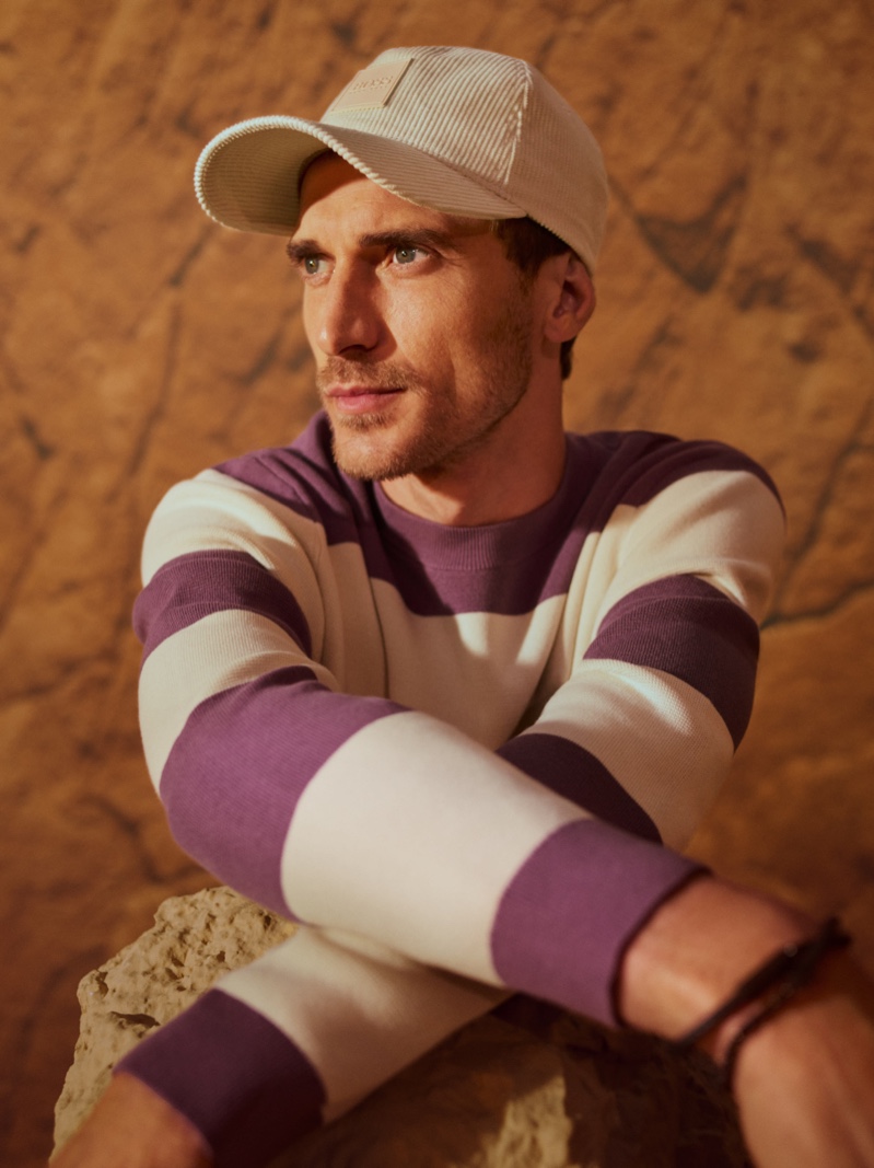 Going casual, Clément Chabernaud models a purple and white striped sweater with a corduroy cap for BOSS's fall-winter 2021 men's campaign.