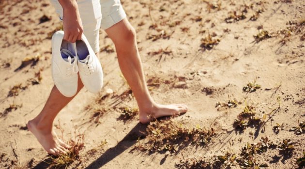 The Best Shoes to Pack for Your European Vacation Man Holding Sneakers Walking Ground Barefoot