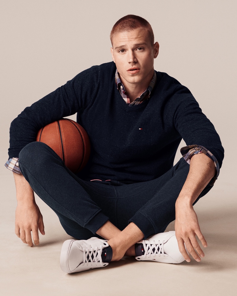 Matthew Noszka dons a navy v-neck sweater and joggers with a plaid shirt for Tommy Hilfiger's fall 2021 men's campaign.