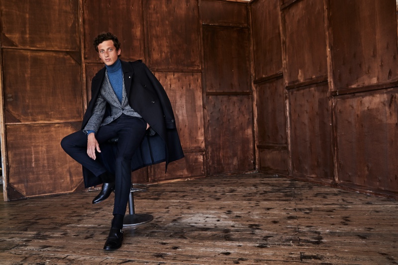 Donning a coat draped over his shoulders, Alexis Maçon-Dauxerre also models a check suit jacket and turtleneck from Luigi Bianchi Mantova.