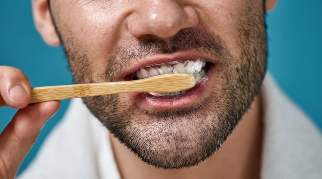 3 Tips to Incorporate Sustainability Into Your Life Man Brushing Teeth with Wooden Toothbrush Closeup