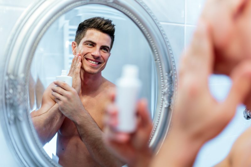 Mens Skincare Man Smiling in Mirror with Product