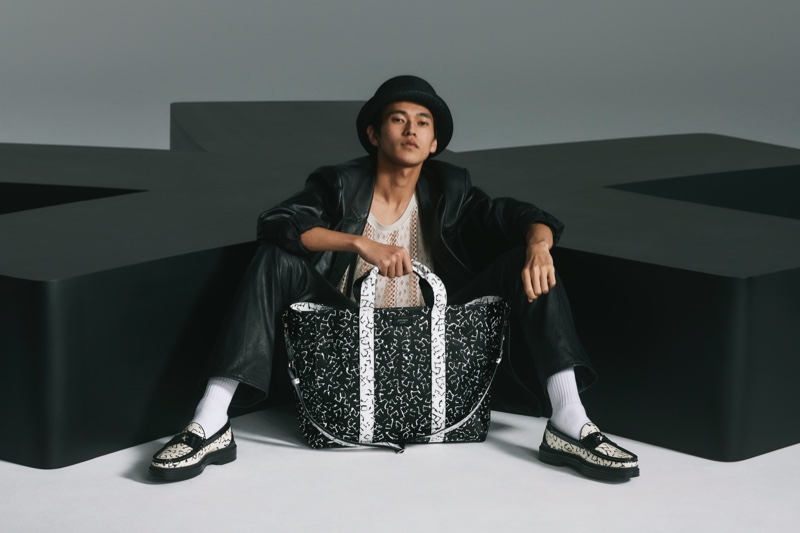 Posing with an oversized bag, Yudai Tateishi wears printed black and white loafers from the Jimmy Choo x Eric Haze collection.