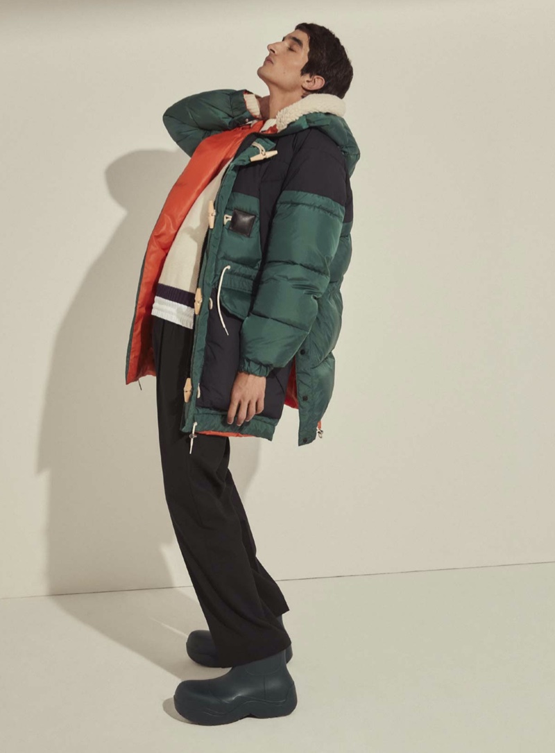 Connecting with Mytheresa for winter, Pablo Fernandez sports a Sacai padded hooded parka, Acne Studios wool-blend mittens, Sacai wool-blend belted pants, and a Sacai knitted intarsia wool-blend sweater.