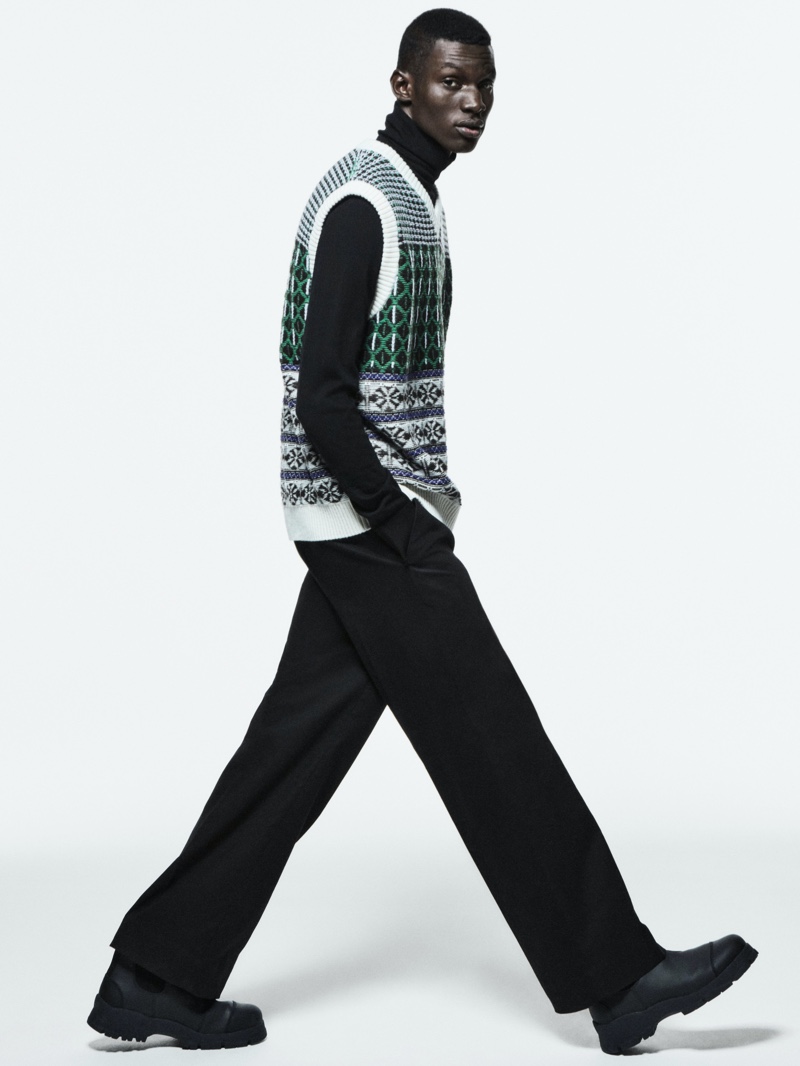 Donning a sweater vest over a turtleneck with wide-leg trousers, Momo Ndiaye appears in COS's holiday 2021 campaign.