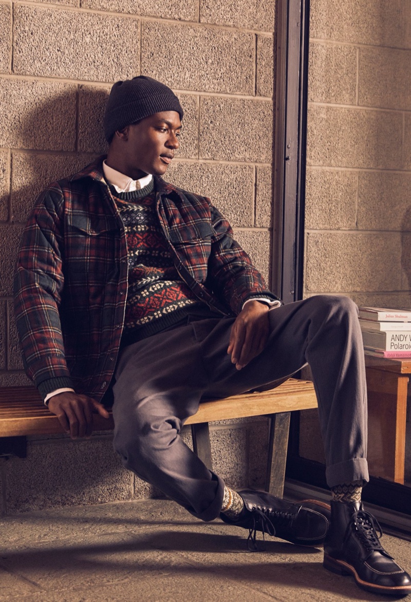 Mixing prints, Hamid Onifade wears a Todd Snyder Italian quilted shirt jacket in wool tartan with a lambswool fair isle sweater, Japanese selvedge oxford button-down shirt, Italian recycled cashmere beanie, slim-fit tab front stretch chinos, and Alden Indy boots.