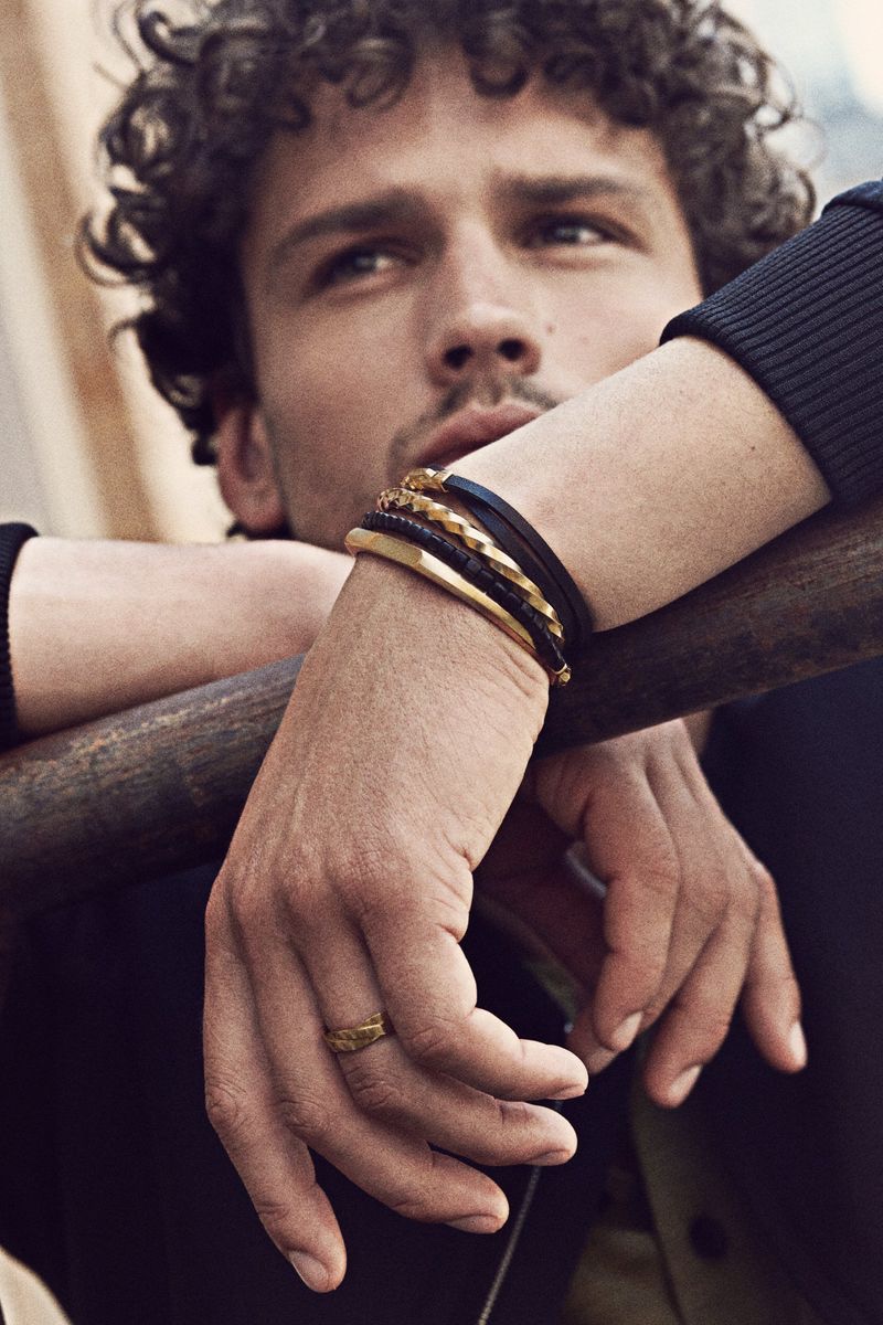 Model Simon Nessman wears multiple David Yurman pieces, including a twisted cable cuff bracelet and a band ring in 18K yellow gold for the brand's fall-winter 2021 campaign.