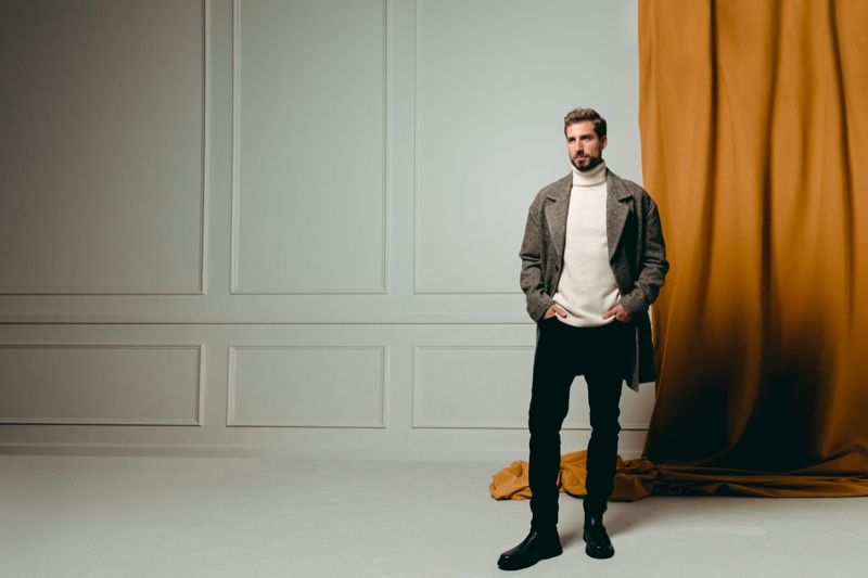 Wearing a herringbone coat and turtleneck sweater, Kevin Trapp showcases pieces from his ABOUT YOU collection.