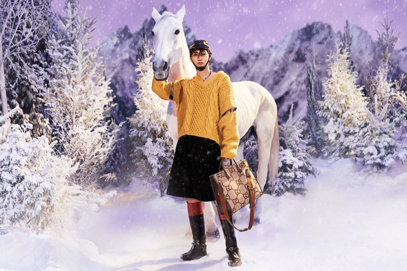 Sporting an oversized cable-knit sweater and riding boots, Kai poses with a horse for the Gucci Aria holiday 2021 campaign.