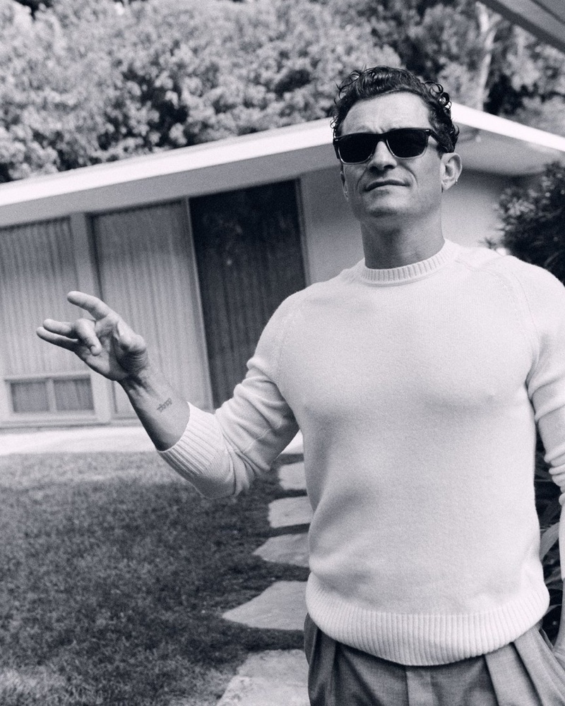 Donning BOSS wayfarer sunglasses, Orlando Bloom wears a Hugo Boss sweater with pleated trousers for Esquire.