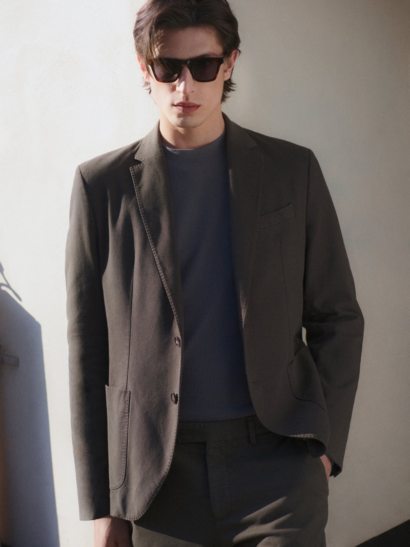 Model Edoardo Sebastianelli sports sunglasses and dons an unlined blazer with trousers and a knit sweater from Massimo Dutti.