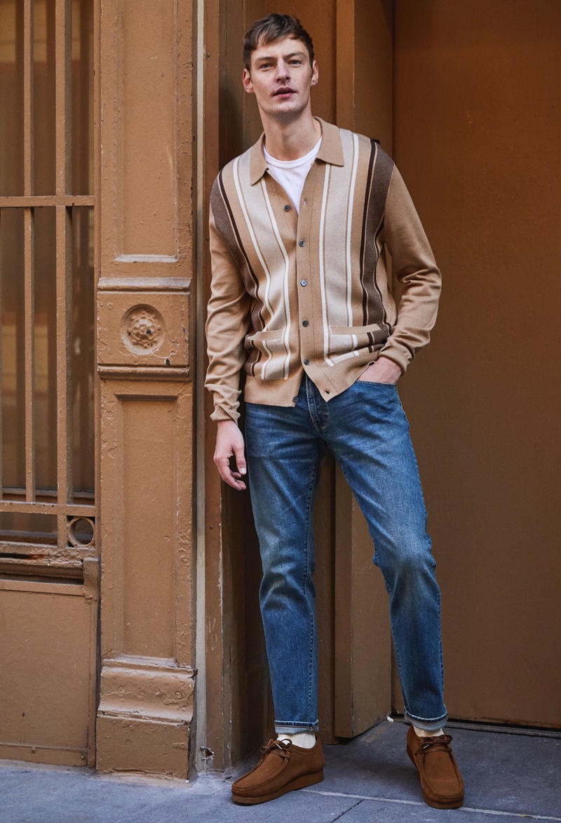 Roberto Sipos trägt ein Poloshirt mit vertikalen Streifen, ein T-Shirt aus Premium-Jersey von Made in LA und eine schmal geschnittene Selvedge-Jeans in mittelblauer Waschung von Todd Snyder mit Clarks Wallabee-Stiefeln.