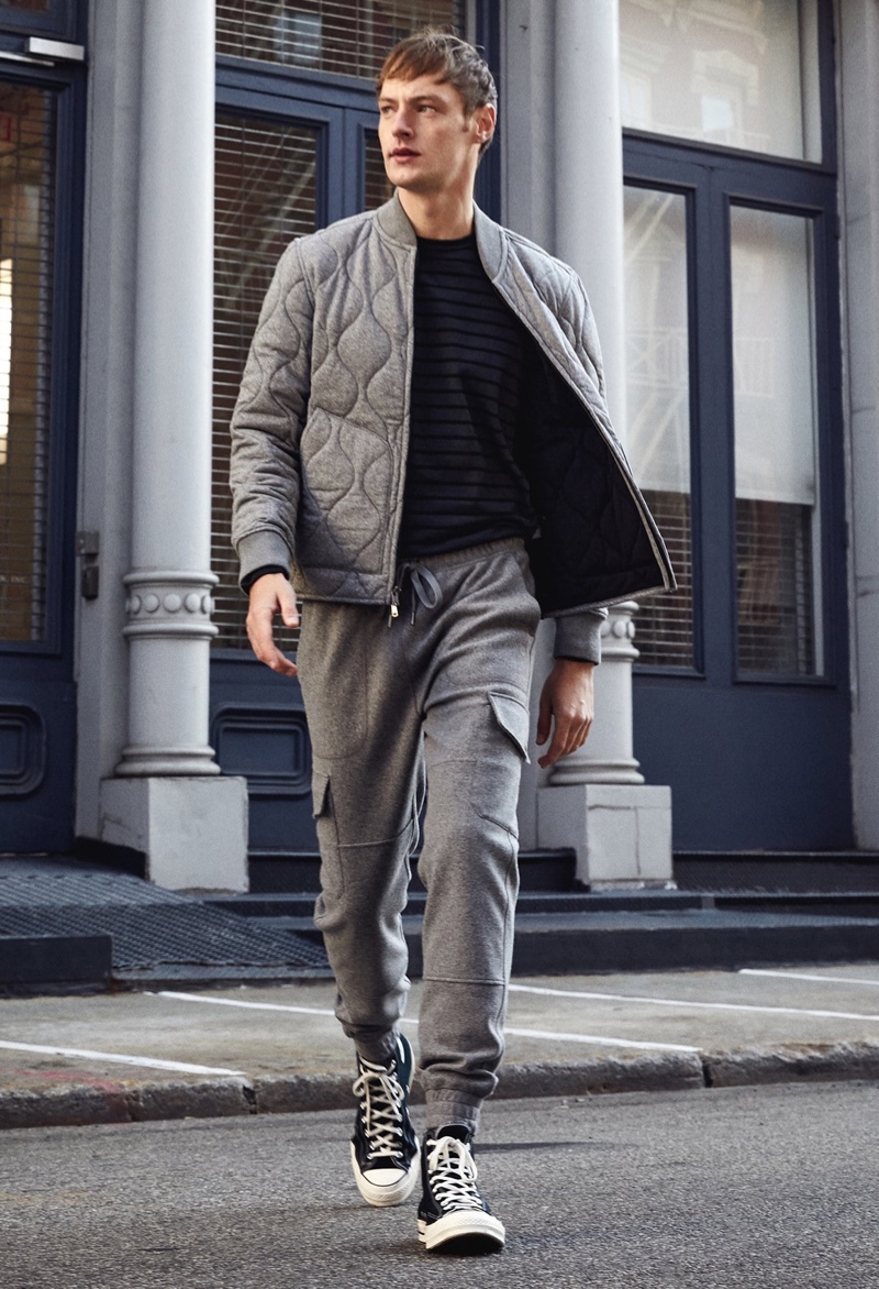 Embracing leisure style in gray, Roberto Sipos dons a Todd Snyder quilted bomber jacket with an Issued by: Japanese nautical striped tee, and military cargo joggers with Converse Chuck 70 high top sneakers.