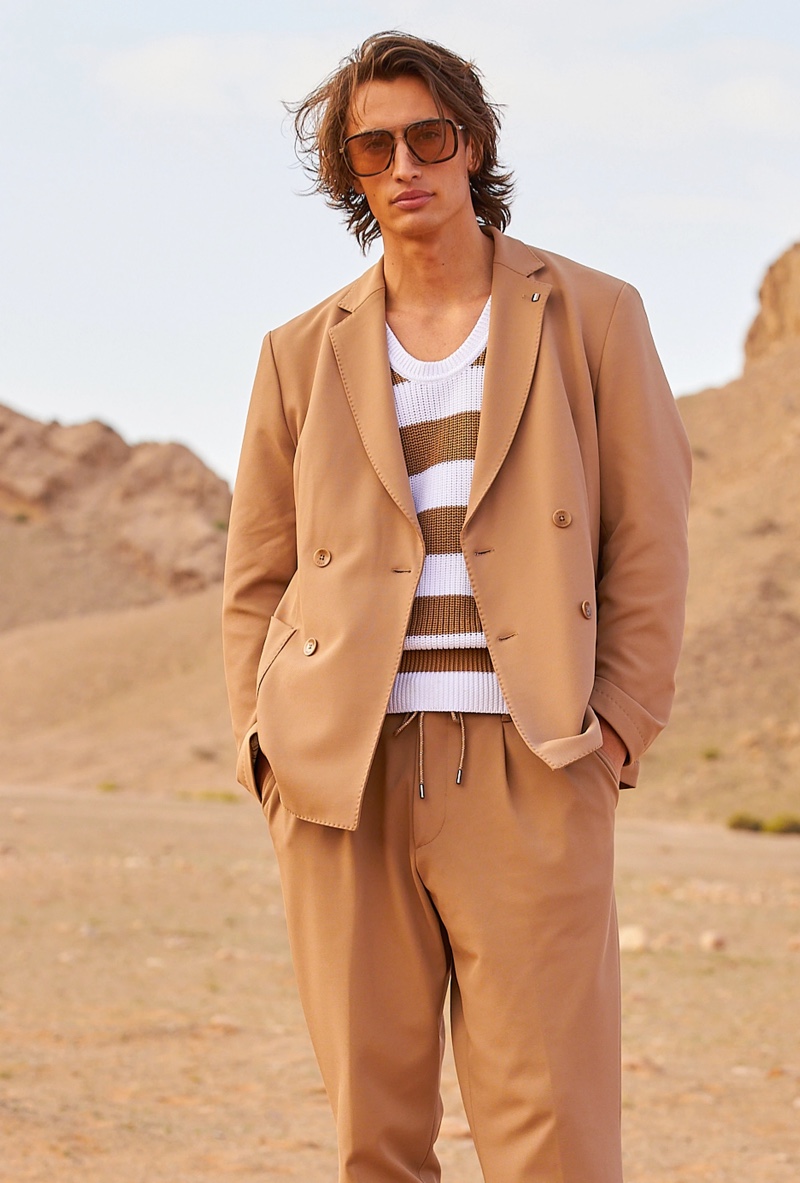 James Turlington models a tan double-breasted BOSS suit with a striped knit sweater.