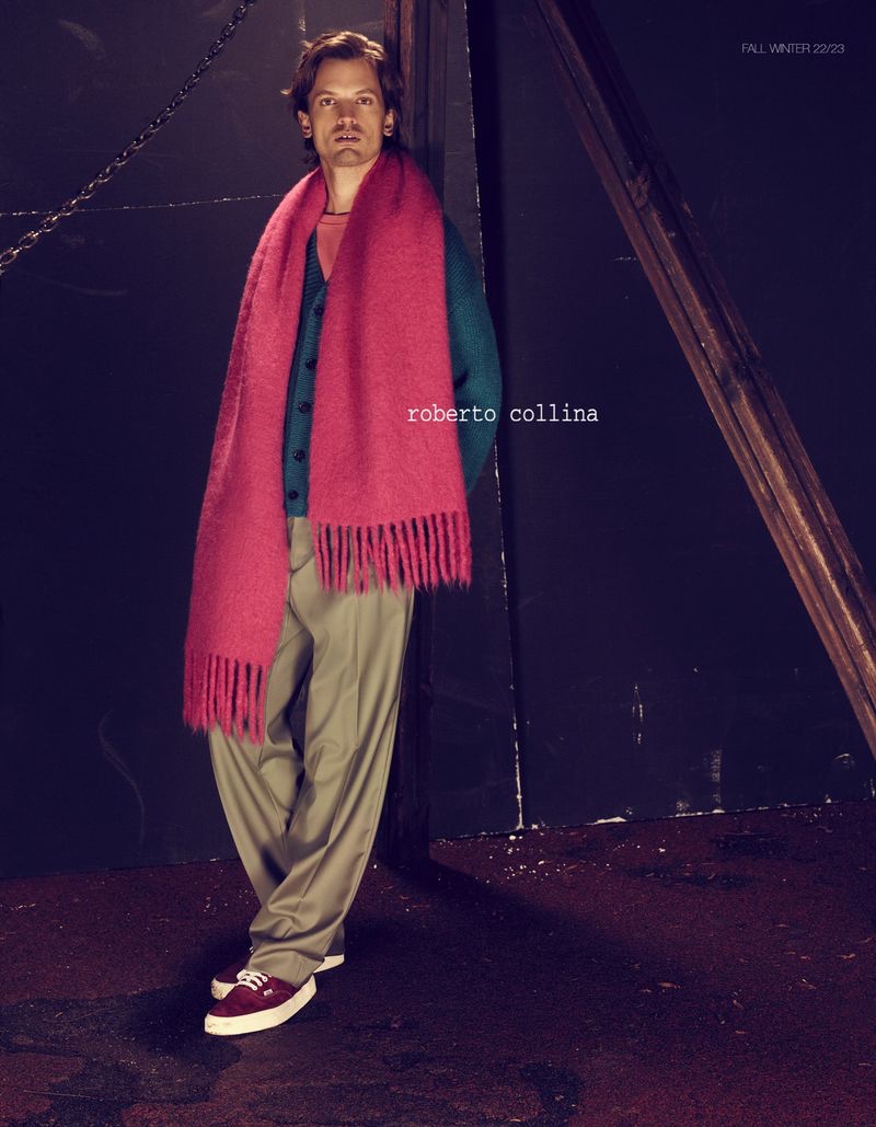 Embracing a splash of color, Eddie Klint wears an oversized scarf with a cardigan sweater from Roberto Collina's fall-winter 2022 collection.