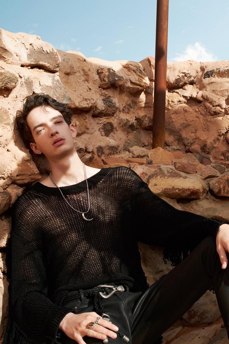 Embracing all black, Kodi Smit-McPhee wears a black open knit fringe sweater with black leather pants, a silver horn necklace, and rope belt for Zara Man's spring-summer 2022 Studio collection campaign.