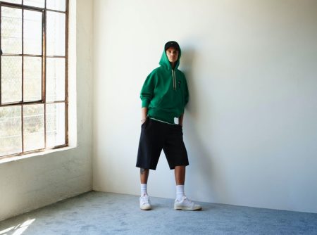 Romeo Beckham sports a green hoodie, oversized shorts, and white leather sneakers for the PUMA x AMI campaign.