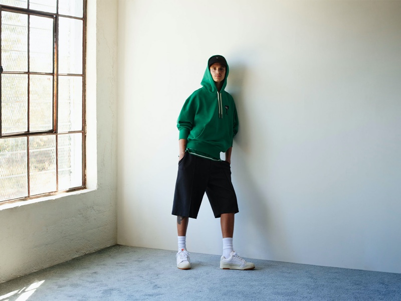 Romeo Beckham sports a green hoodie, oversized shorts, and white leather sneakers for the PUMA x AMI campaign.