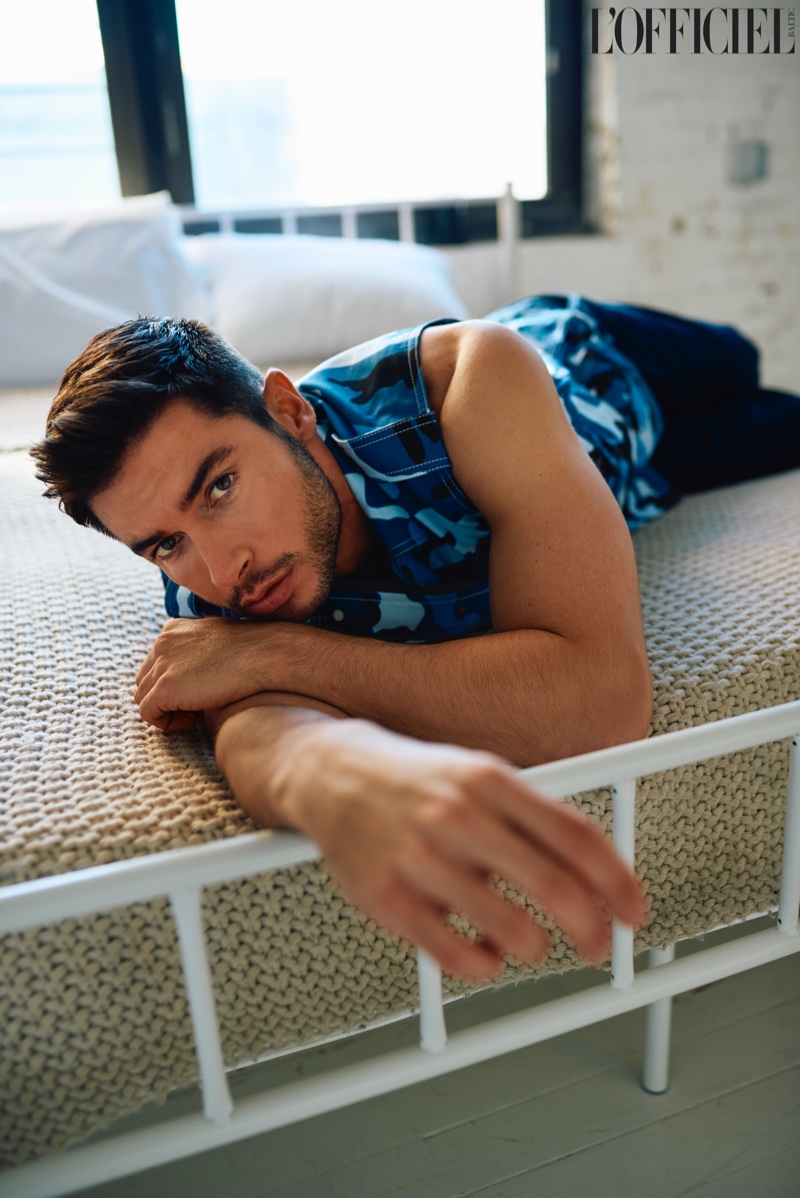 Laying in bed, Andrea Denver wears a camouflage Valentino vest with Max & Chester pants.