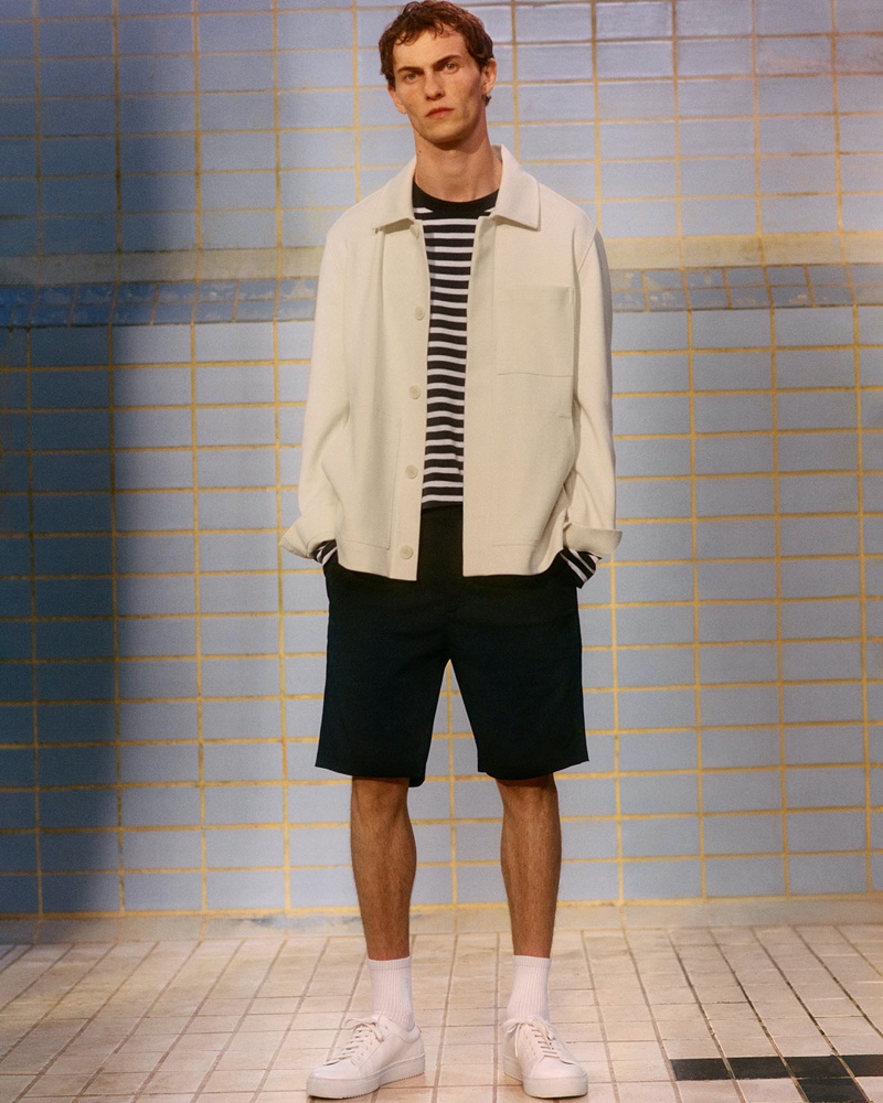 Connecting with COS for spring, Luc Defont-Saviard wears a workwear jacket with a striped long-sleeve top and shorts.