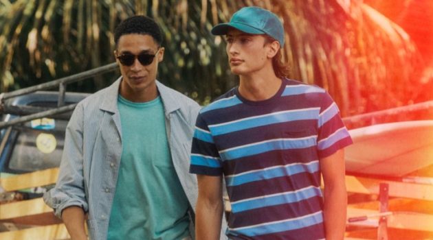 James & Luke Embrace Summer Style in J.Crew Left: Luke Cousins wears a J.Crew secret wash striped poplin shirt with a garment-dyed pocket t-shirt, drawstring pants, Bungalow sunglasses, and Birkenstock Arizona sandals. Right: James Turlington models a J.Crew striped pocket t-shirt, camp pants in yellow, a garment-dyed twill baseball cap, striped elastic webbing belt, and Adidas Gazelle suede sneakers.