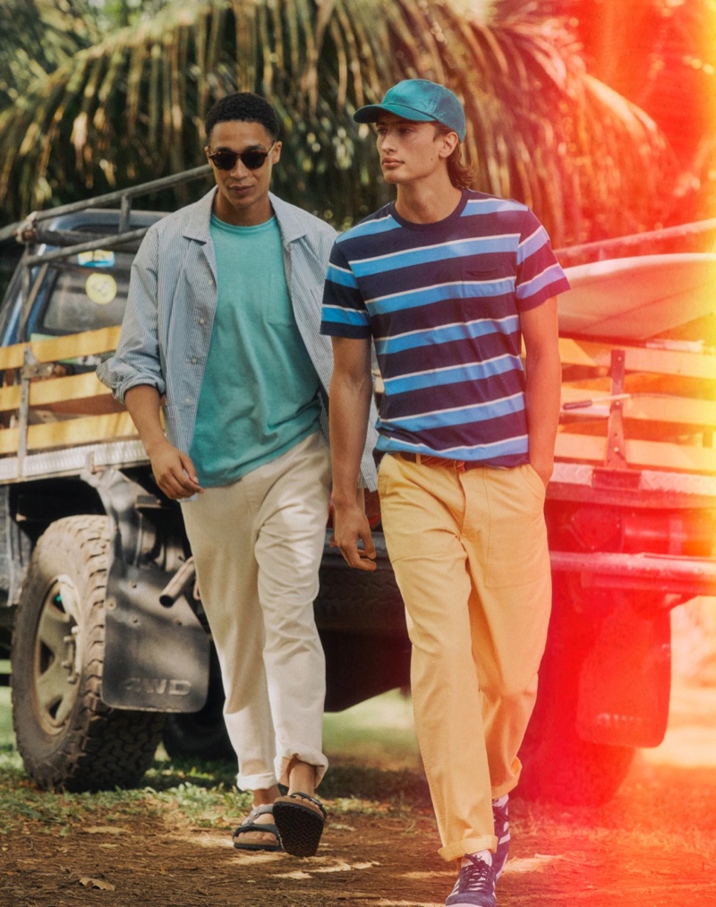 Left: Luke Cousins wears a J.Crew secret wash striped poplin shirt with a garment-dyed pocket t-shirt, drawstring pants, Bungalow sunglasses, and Birkenstock Arizona sandals. Right: James Turlington models a J.Crew striped pocket t-shirt, camp pants in yellow, a garment-dyed twill baseball cap, striped elastic webbing belt, and Adidas Gazelle suede sneakers.