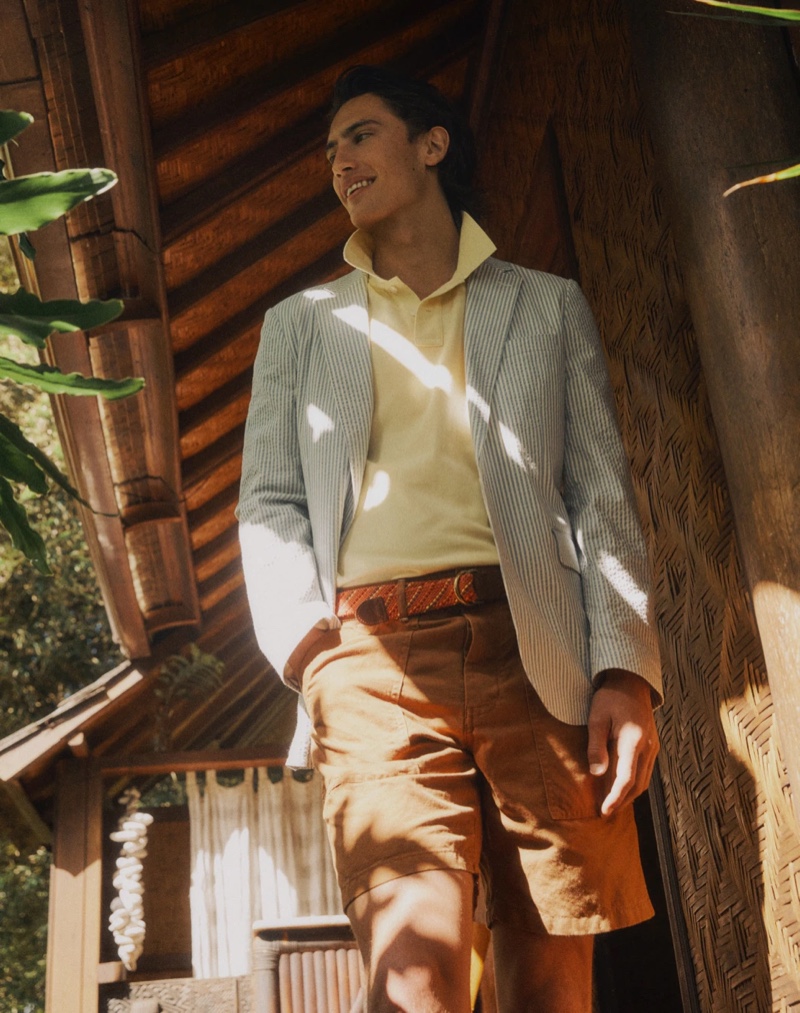 Showcasing preppy style, James Turlington dons a Ludlow slim-fit unstructured suit jacket in seersucker with yellow piqué polo shirt, 8" camp shorts, and a D-ring webbed belt from J.Crew.