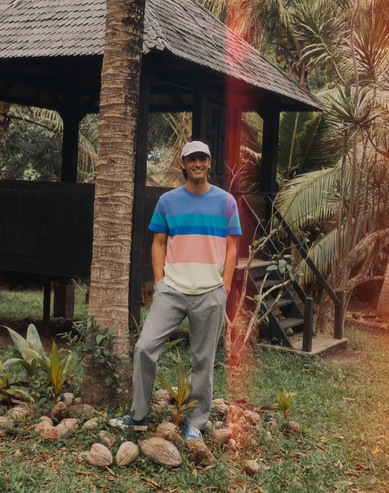 All smiles, James Turlington wears a J.Crew rugby striped shirt with pleated chino pants in stretch cotton-linen, a garment-dyed twill baseball cap, and Collective Canvas Vier sneakers.