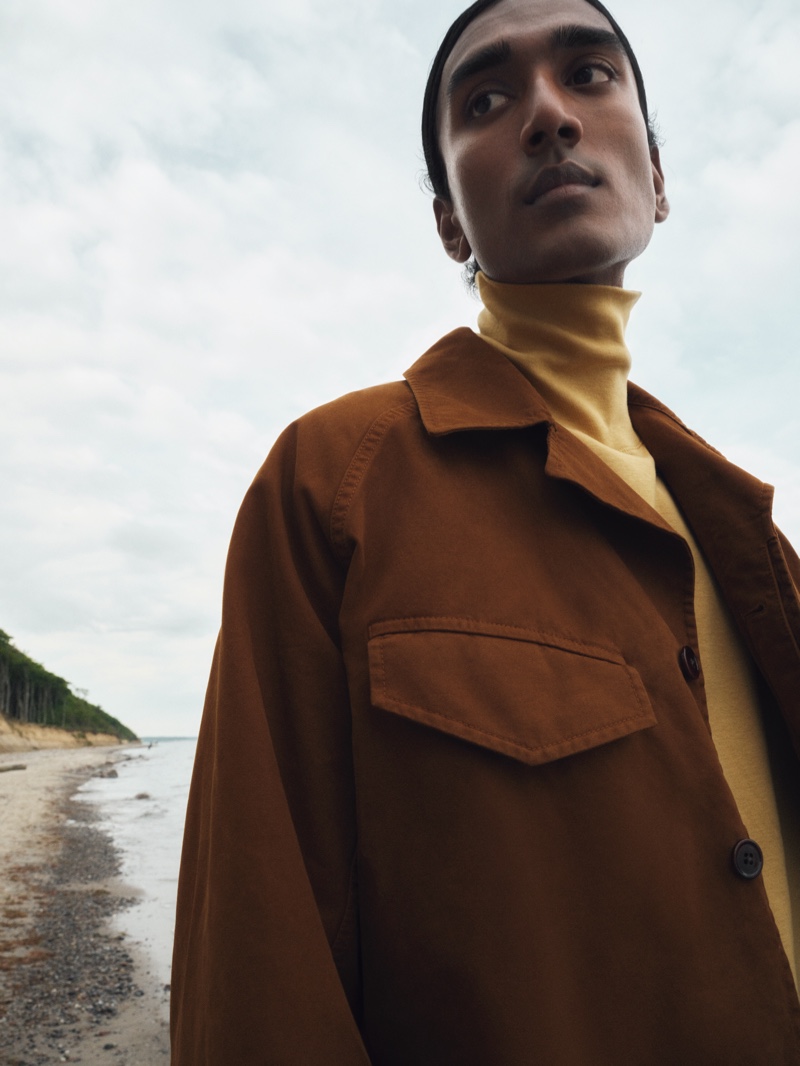 Francois Delacroix wears a yellow cotton jersey turtleneck top and a brown canvas jacket from the LEMAIRE x Mytheresa collection. 